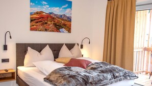 A bedroom with a large bed, a headboard, two wall-mounted lamps, a nightstand, and a window with curtains. - Exquisite flat with sauna on the piste (Weißpriach)