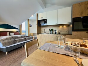 A modern hotel room with a bed, a wooden dining table with a placemat, a pitcher of water, and a glass of water.