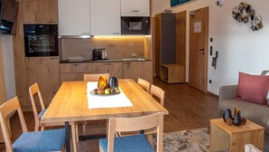 A compact kitchen with modern appliances, a dining area with a wooden table and blue cushioned chairs, and a living space with a sofa and decorative items. - Exquisite flat with sauna on the piste (Weißpriach)