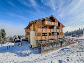 A multi-story wooden chalet with balconies, a glass enclosure, and a ski lift in the background.