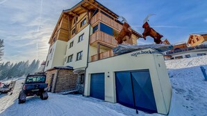 A multi-story building with wooden balconies, a covered garage, and a snow-covered ground. - Exquisite flat with sauna on the piste (Weißpriach)