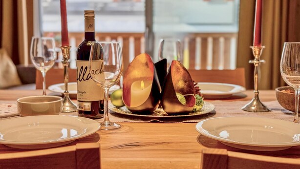 A dining table set with plates, glasses, a bottle of wine, and candles. - Luxurious apartment with a sauna on the slope (Weißpriach)