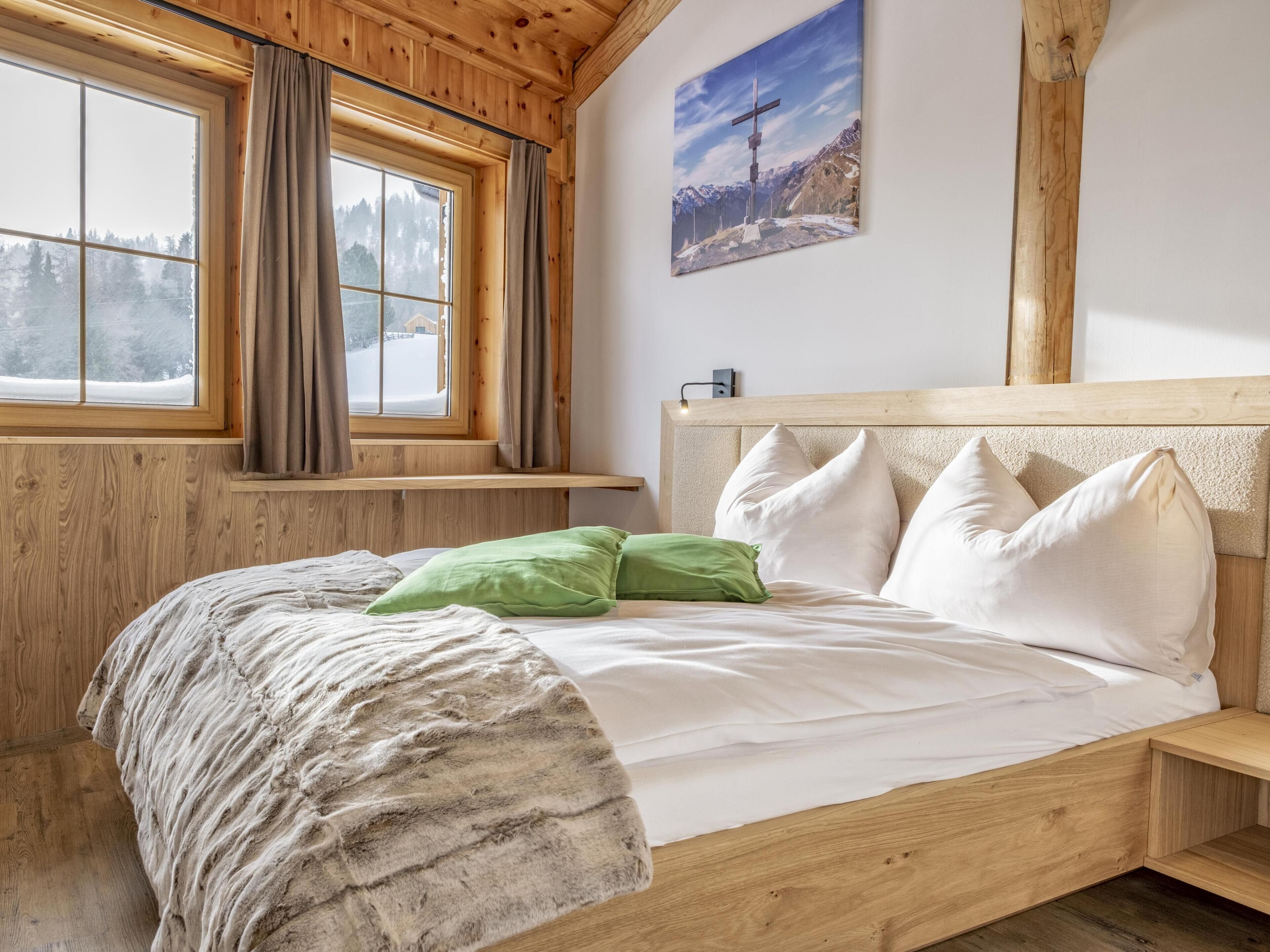 Una cama de madera con cabecera, una ventana con cortinas y un cuadro en la pared.