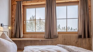 Een gezellig slaapkamer met een houten hoofdeinde, een raam met gordijnen en uitzicht op met sneeuw bedekte bomen.