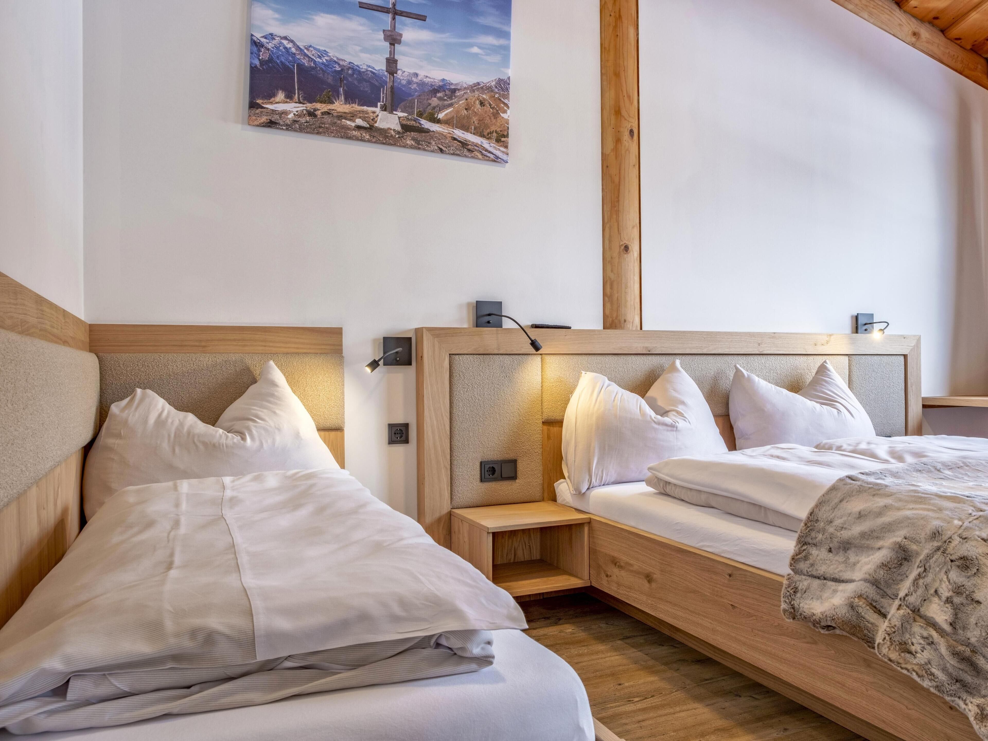 A bedroom with two beds, wooden headboards, bedside tables, and a wall-mounted lamp.
