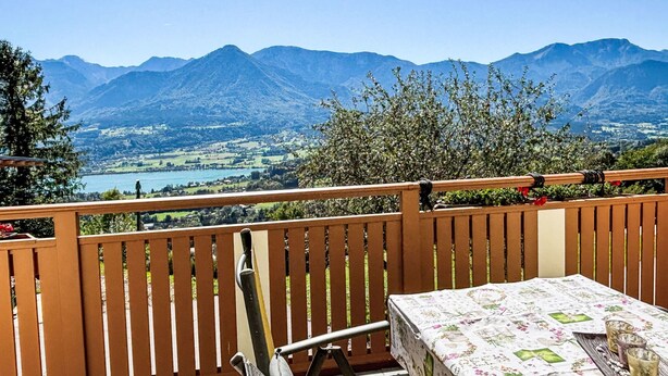 A balcony with a wooden railing, a table with a floral tablecloth, and a view of mountains and a lake. - Hochstuhlblick by Interhome (Ludmannsdorf)