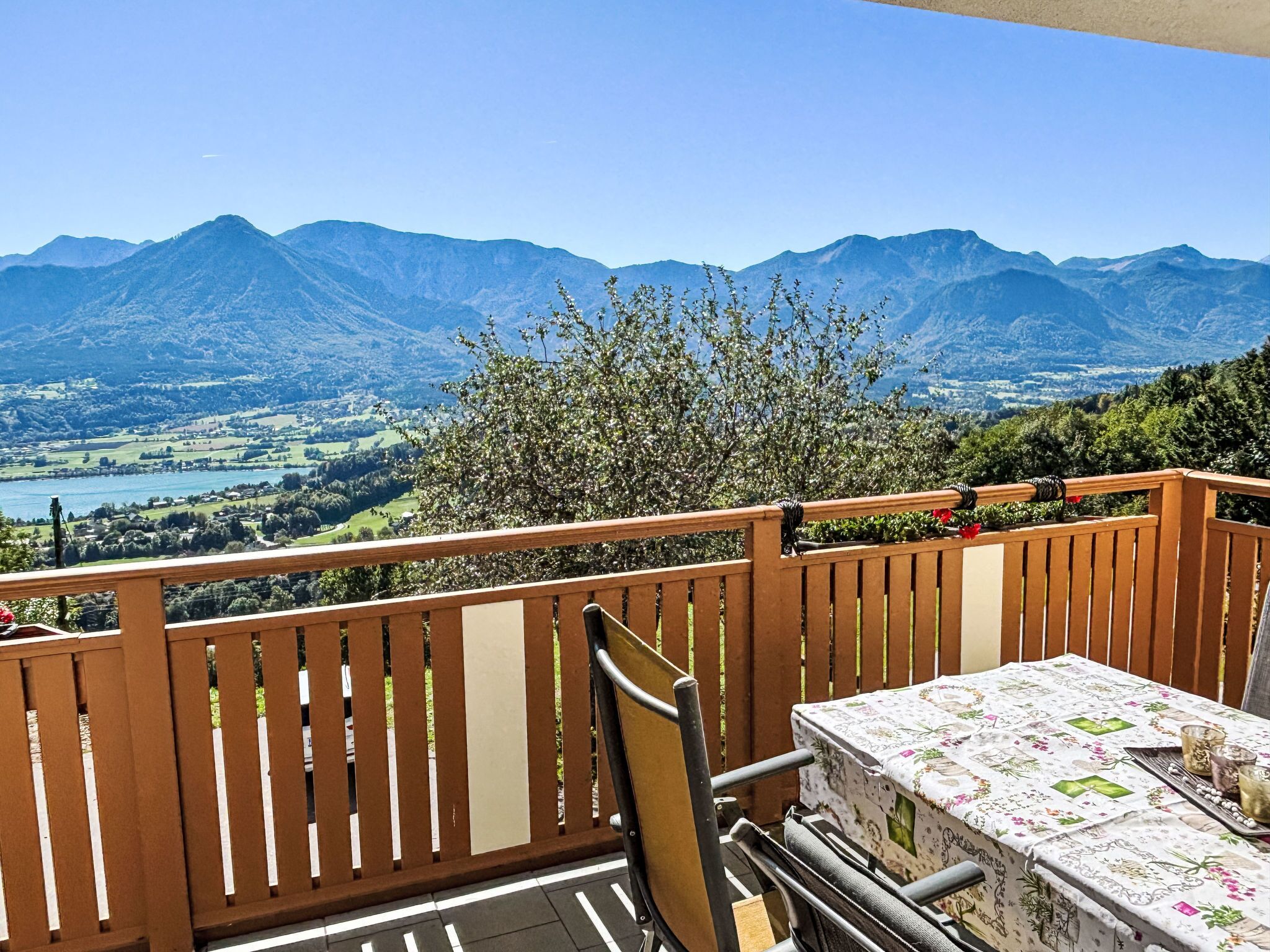 Un balcon avec une table et des chaises, donnant sur un paysage montagneux avec un lac.