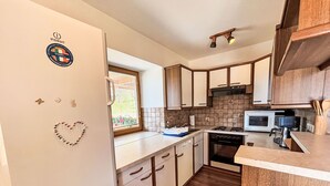 A compact kitchen with wooden cabinets, a microwave, and a stove. - Hochstuhlblick by Interhome (Ludmannsdorf)