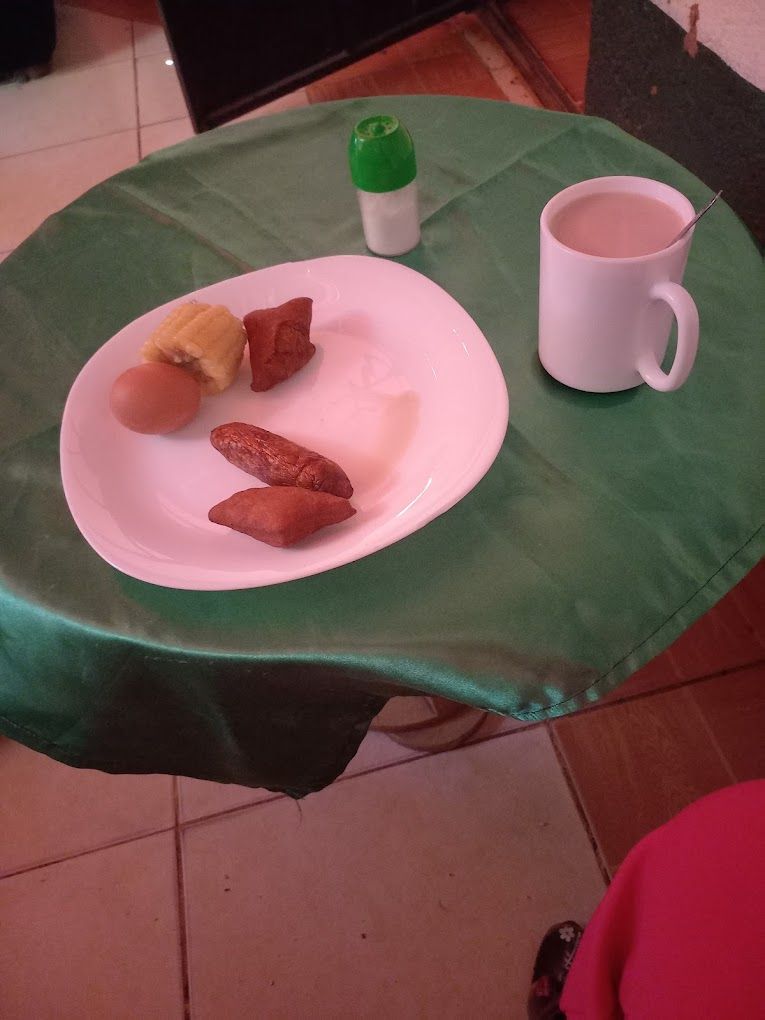 Una mesa con mantel verde, un plato blanco con comida, una taza blanca y una botella verde.