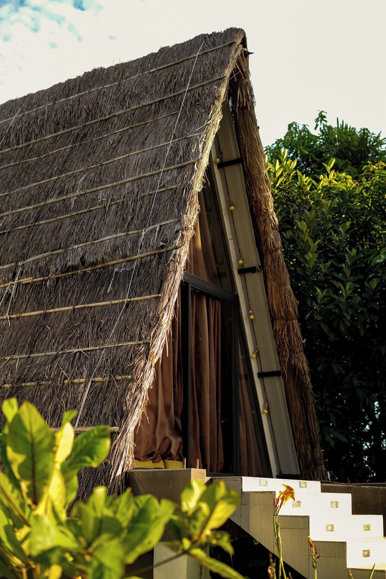 A traditional thatched-roof structure with a sloped roof and a window with curtains.