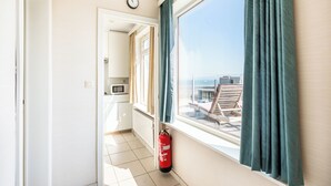 A corridor leading to a balcony with a view of the sea, a fire extinguisher, and a clock on the wall.