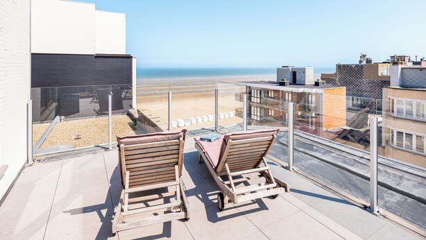 A balcony with two wooden lounge chairs facing a beach view.