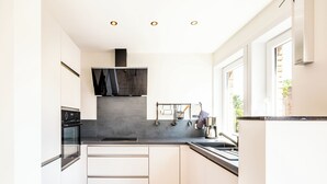 A modern kitchen with white cabinets, a black countertop, and a built-in oven. - Renovated flat centrally located (Koksijde)