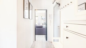 A narrow hallway with a white wall, a grey sofa in the background, and a white cabinet with multiple drawers. - Renovated flat centrally located (Koksijde)