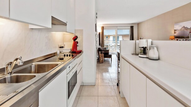 A modern kitchen with stainless steel appliances, a red coffee machine, and a view to a balcony.