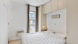 A bedroom with a bed, a nightstand, a wall-mounted lamp, and a window with curtains.