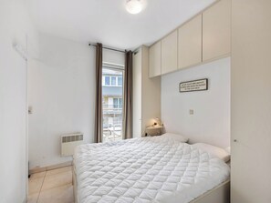 A bedroom with a bed, a nightstand, a wall-mounted lamp, and a window with curtains.