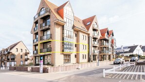 A modern apartment building with multiple balconies, a parking area, and a clear sky. - Beautifully renovated flat with sea views (Koksijde)