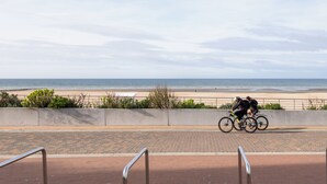 A paved path with metal railings, leading to a beach with a cyclist. - Beautifully renovated flat with sea views (Koksijde)