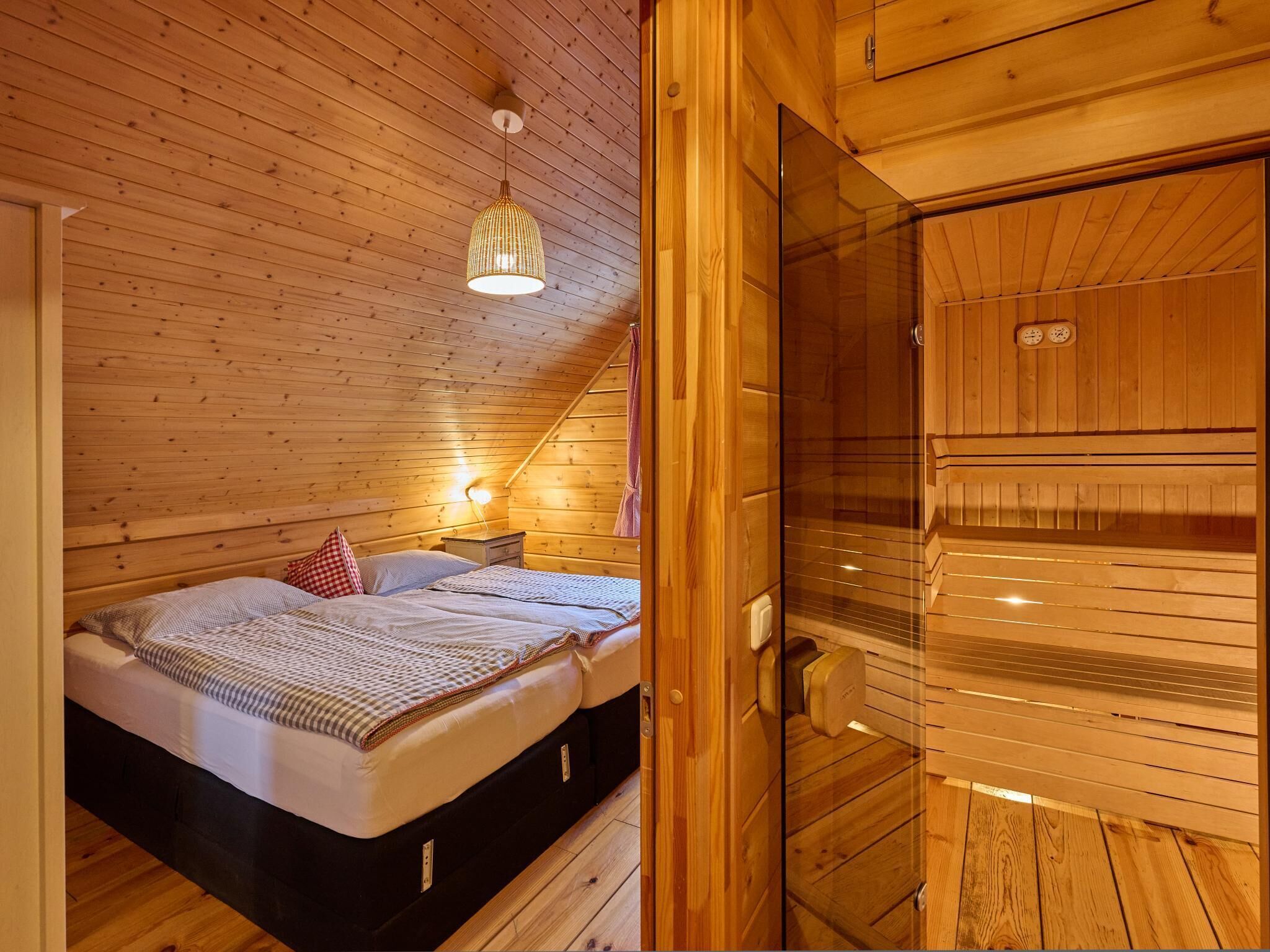 Ein gemütliches Holzblockhaus-Zimmer mit Bett, einer Hängeleuchte und einer Saunatür.