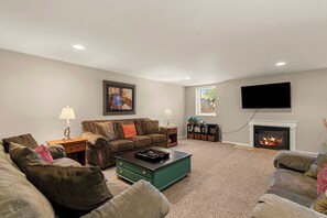 A living room with a fireplace, a television mounted on the wall, and a bookshelf. - Near Leavenworth Riverfront 6BR + Hot Tub Retreat (Peshastin)