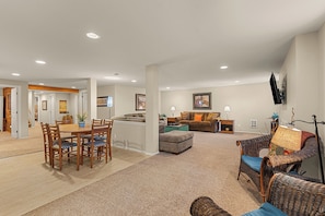 A spacious living room with a dining area, a sofa set, and a television mounted on the wall.