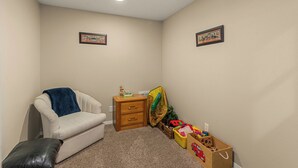 Una habitación pequeña con alfombra, un sofá blanco, una mesita de madera y un baúl para guardar juguetes.