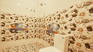 A bathroom with a pebble-patterned wall and floor, a white toilet, and a shower area. - Neev Haveli (Udaipur)