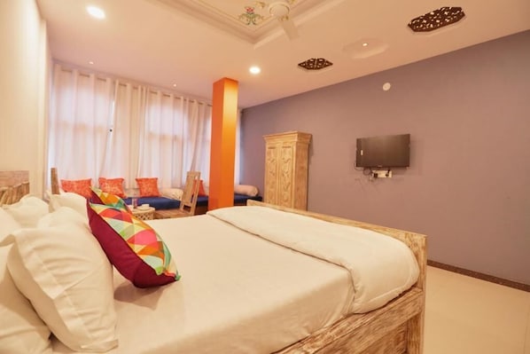 Un dormitorio con una cama grande, televisor montado en la pared y una ventana con cortinas.
