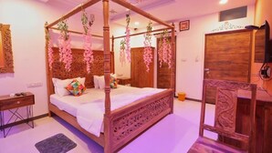 A four-poster bed with hanging pink flowers, a wooden wardrobe, and a television on the wall. - Neev Haveli (Udaipur)