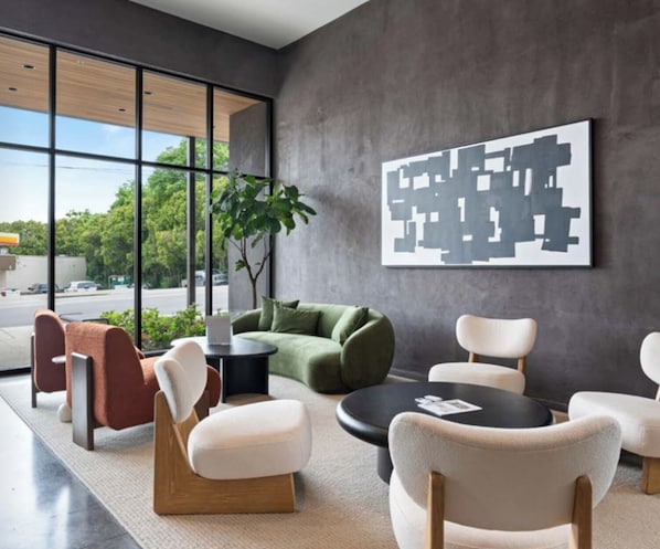 A modern interior with a green sofa, white armchairs, and a round table. A large abstract painting is on the wall, and there's a plant in the corner. - Landing Apartments Nashville - Inglewood (Nashville)