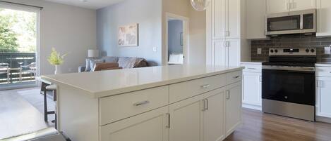 A modern kitchen with white cabinetry, a large island, stainless steel appliances, and a view to the outside.