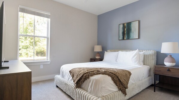 Une chambre à coucher avec un grand lit, deux tables de chevet, une fenêtre et un tableau au mur.