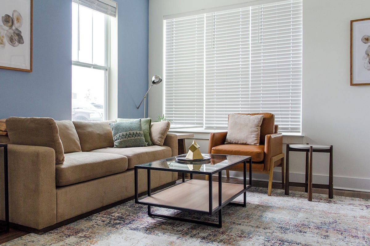 A living room with a beige sofa, a glass coffee table, a brown leather armchair, and a small side table.