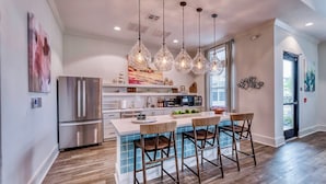 A modern kitchen with a central island, stainless steel appliances, hanging pendant lights, and a view to the outside. - Landing Apartments - Lebanon, IN (Lebanon)