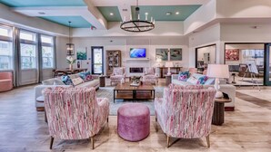 A spacious living room with a large coffee table, patterned armchairs, and a pink ottoman. - Landing Apartments - Lebanon, IN (Lebanon)