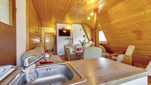 Interior acogedor de una cabaña con techo de madera, una zona de cocina con pileta y encimera, y un área de estar con sofá y sillones.