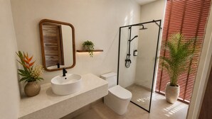 Ein modernes Badezimmer mit rundem Waschbecken, Toilette und einer Duschkabine aus Glas.