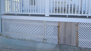 A covered porch with a white railing, a wooden door, and a lattice fence. - Cozy large 2 bedrooms apartment on Historic Mt Auburn • 5 Min to Harvard (Watertown)