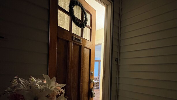 A wooden front door with a wreath, a glass door, and a small table with a vase of flowers. - Cozy large 2 bedrooms apartment on Historic Mt Auburn • 5 Min to Harvard (Watertown)