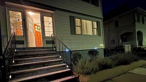 A two-story house with a front entrance, a staircase leading to the door, and a small garden area. - Cozy large 2 bedrooms apartment on Historic Mt Auburn • 5 Min to Harvard (Watertown)