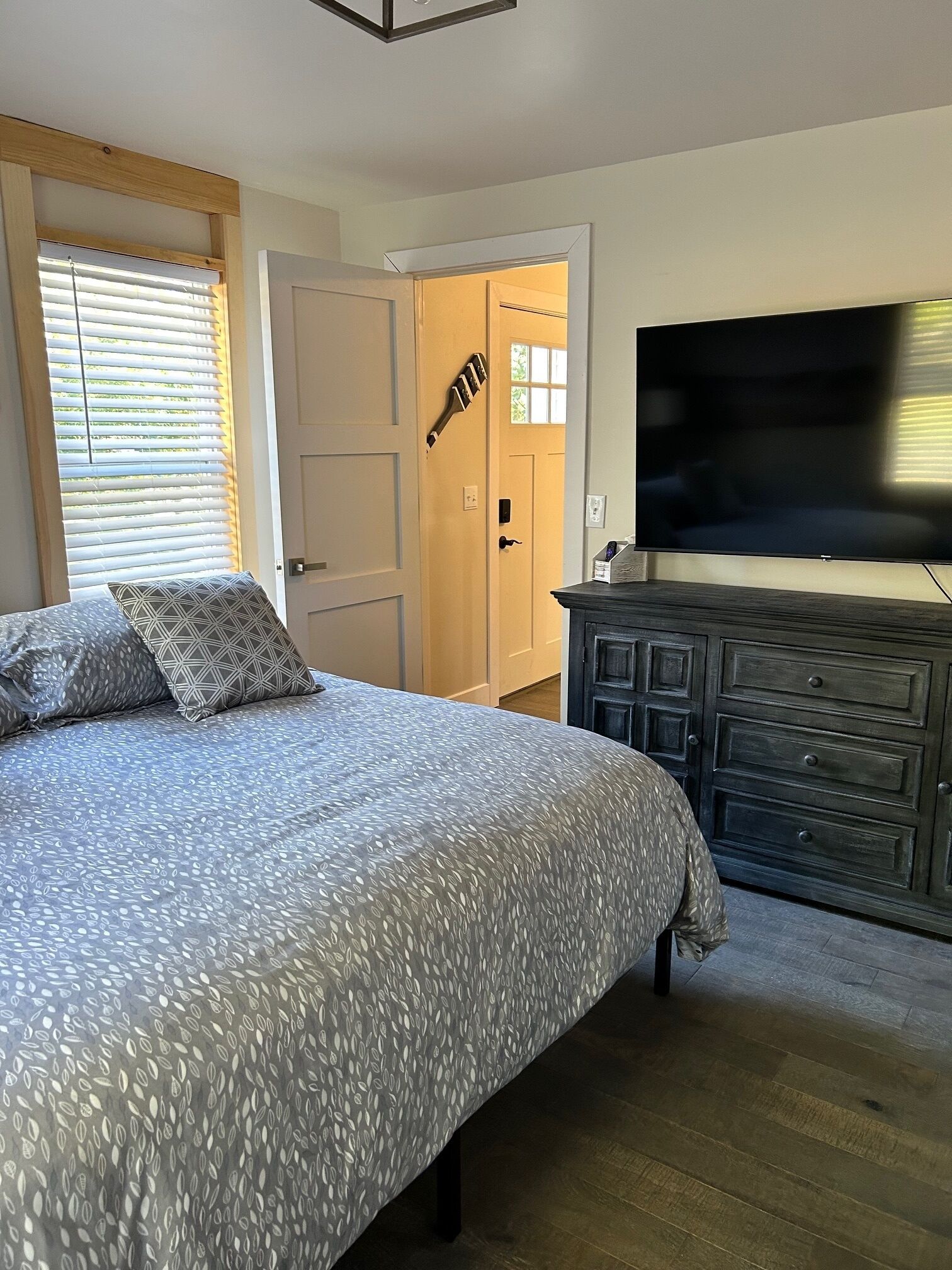 A bedroom with a bed, a dresser, a television, and a door with a window.