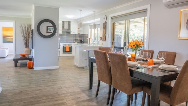 A modern kitchen with white cabinets, a central island, and a dining area with a dark table and brown chairs. - Stays with Ripley,
4bed, 2 bath pet friendly home only 3min drive to Hosp/beach! (Urraween)