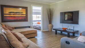 A living room with a sofa, a grey armchair, a coffee table, a TV, and a painting on the wall. - Stays with Ripley,
4bed, 2 bath pet friendly home only 3min drive to Hosp/beach! (Urraween)