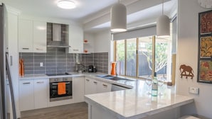 A modern kitchen with white cabinets, a large island, and a view of the backyard. - Stays with Ripley,
4bed, 2 bath pet friendly home only 3min drive to Hosp/beach! (Urraween)