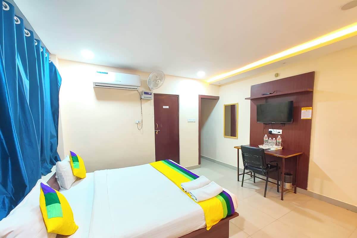 A hotel room with a bed, a desk, a chair, an air conditioning unit, a television, and a door.