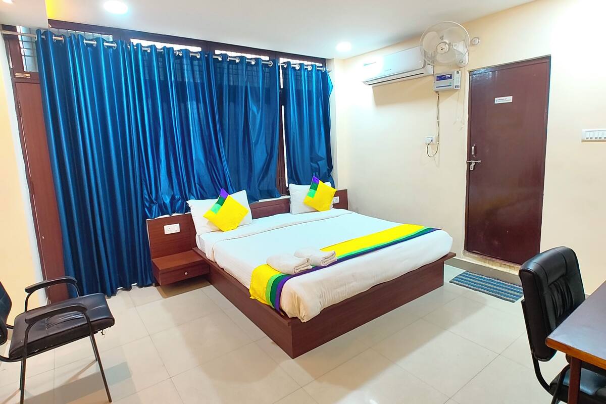 A hotel room with a bed, a desk, a chair, a wardrobe, and a window with curtains.