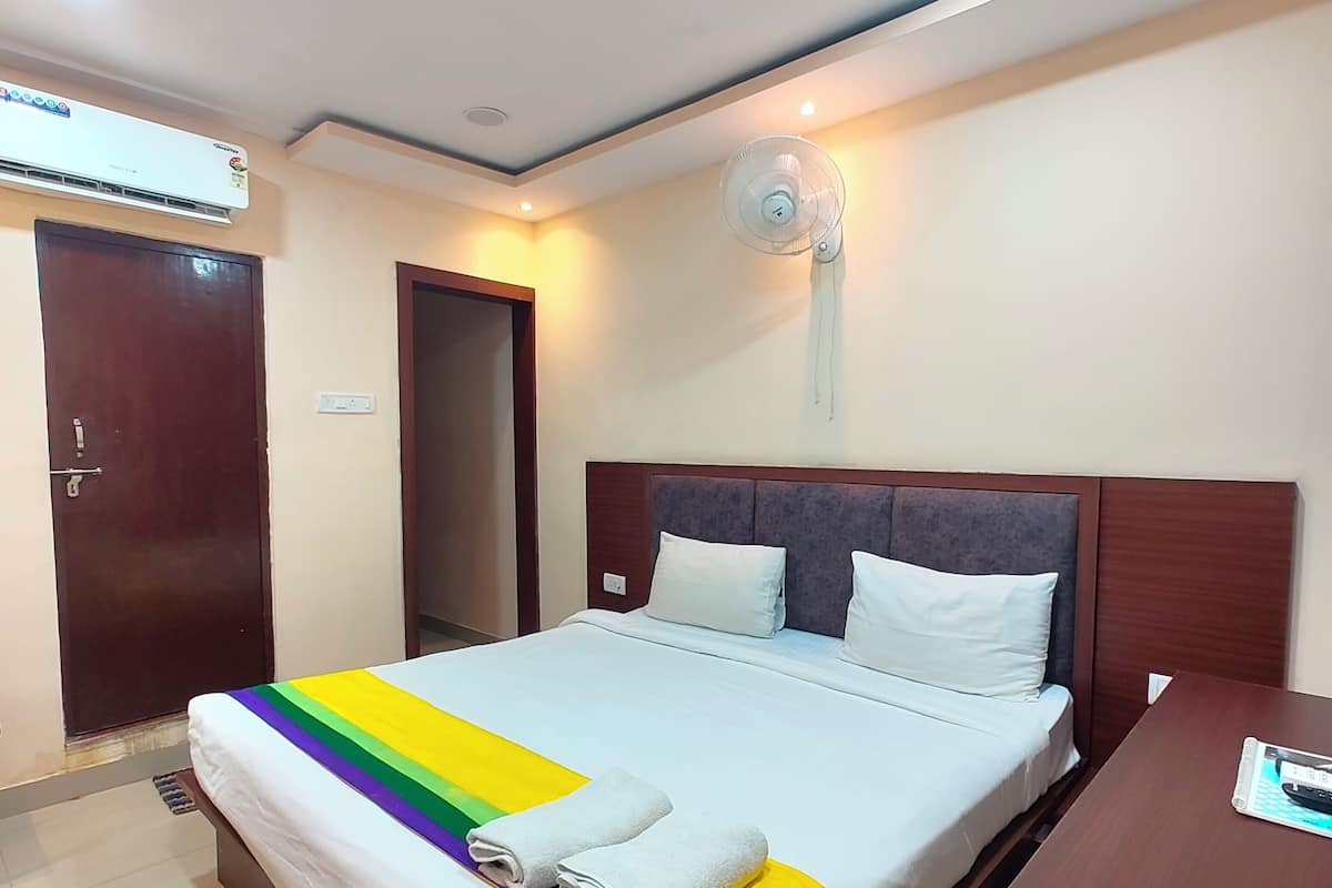 A hotel room with a bed, a wooden headboard, a bedside table, an air conditioning unit, and a ceiling fan.