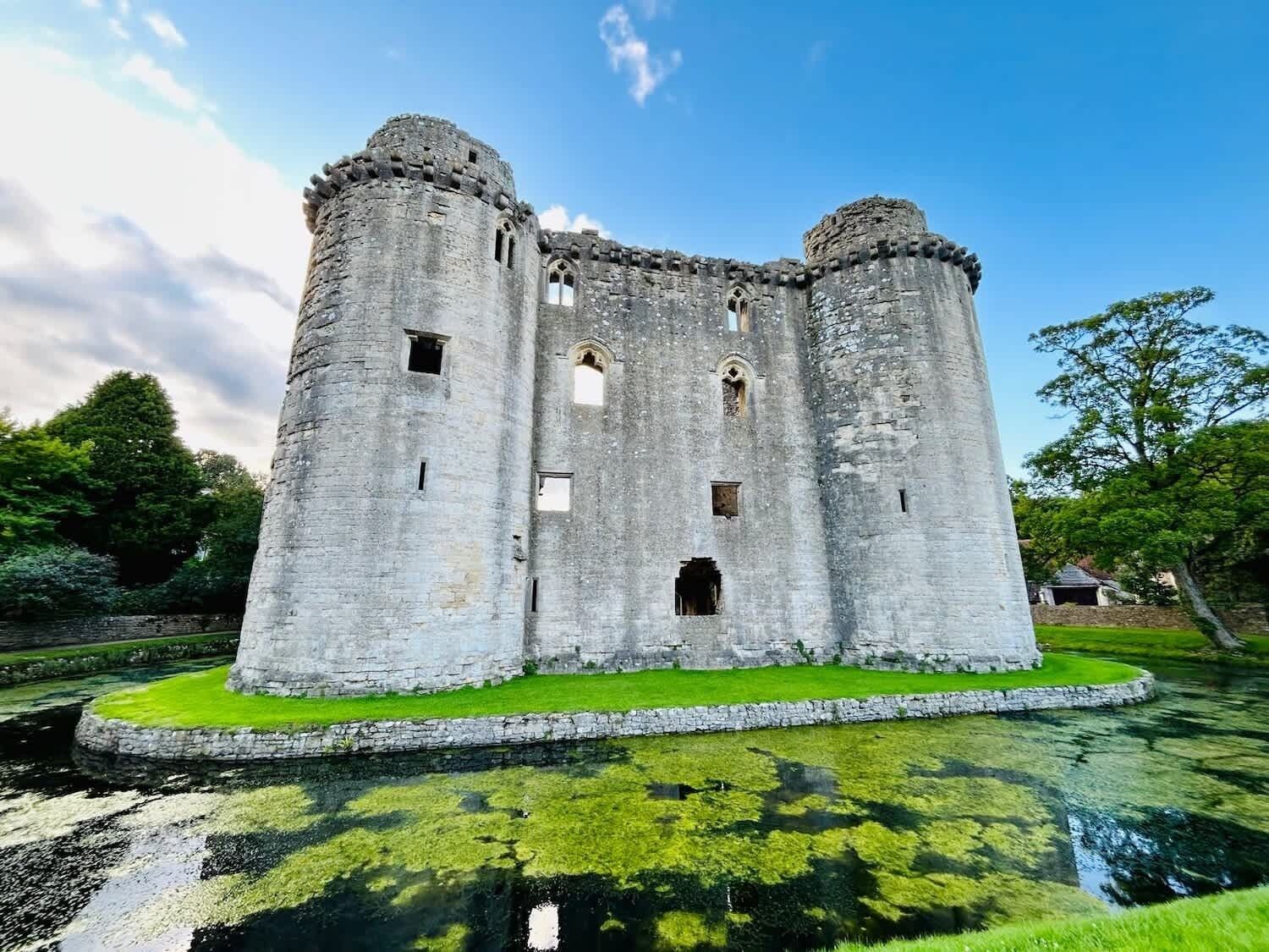 A historic castle with two towers, a moat, and a grassy island.