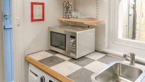 A compact kitchen with a washing machine, a microwave, a sink, and shelves with glassware.